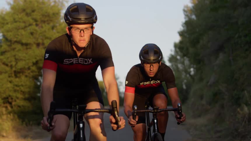 Two men with helmets riding bikes on a road with trees in the background