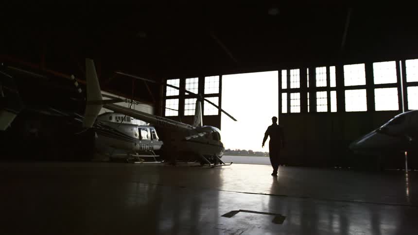 Silhouette of a person walking towards a helicopter inside a hangar
