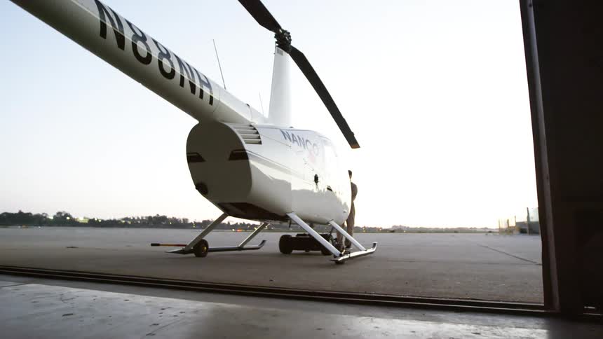 A man pulls a helicopter out of a building and across the tarmac