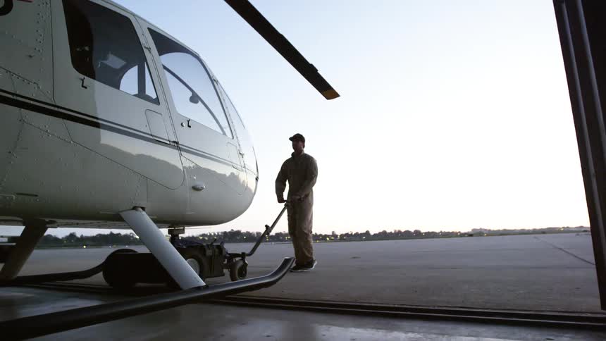 Man rolling out helicopter from hangar to the tarmac