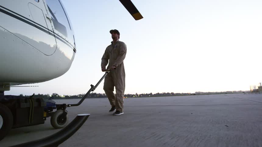 Man pulls helicopter across field toward buildings