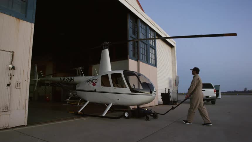 Man pushes a helicopter inside a hangar in an airport at sunset