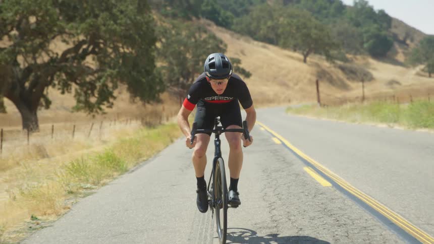 A cyclist rides down a rural two lane rane past hills and fields