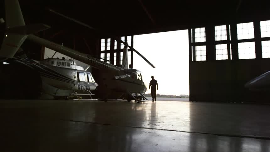 A man walks into a hangar and approaches a helicopter