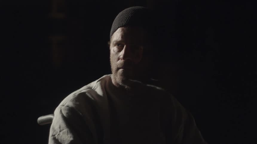 A man sitting down in a dark area looks up to the side