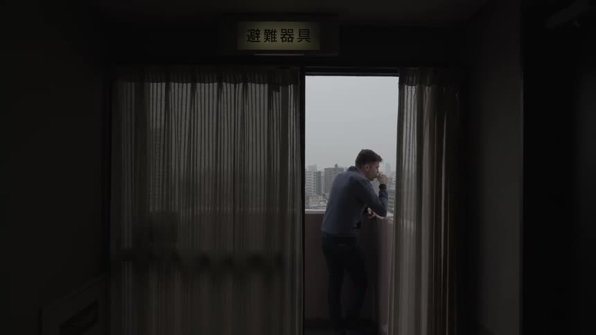 A man sipping a drink on a balcony as he looks over the city