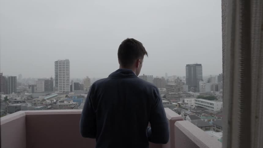 Man standing on a balcony looking out at the city