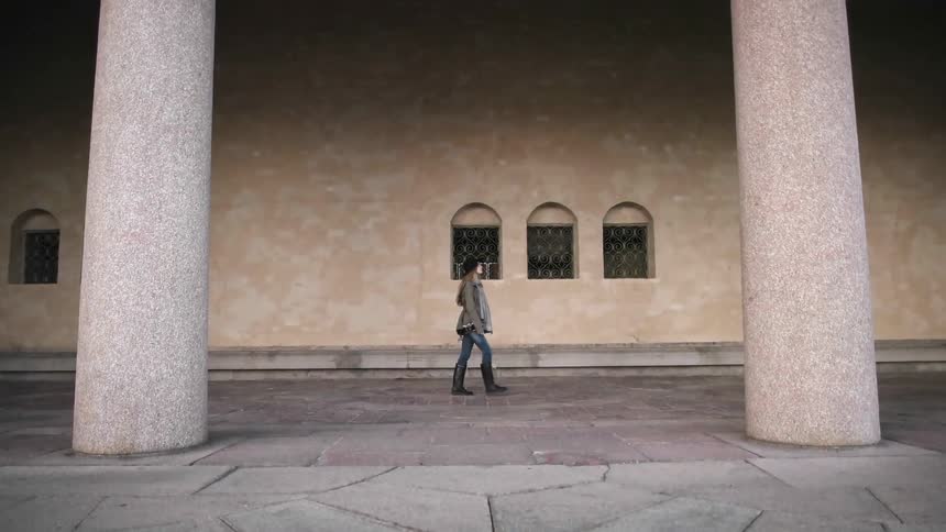A woman is walking past a stone building between two pillars
