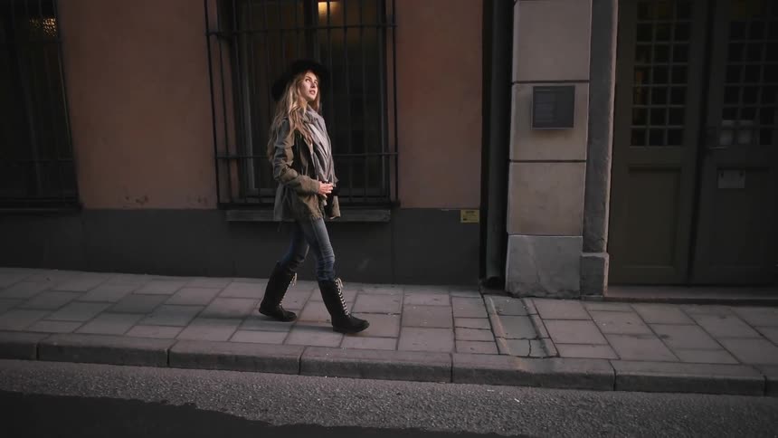 A woman wearing a cowboy hat walks down a cobblestone sidewalk