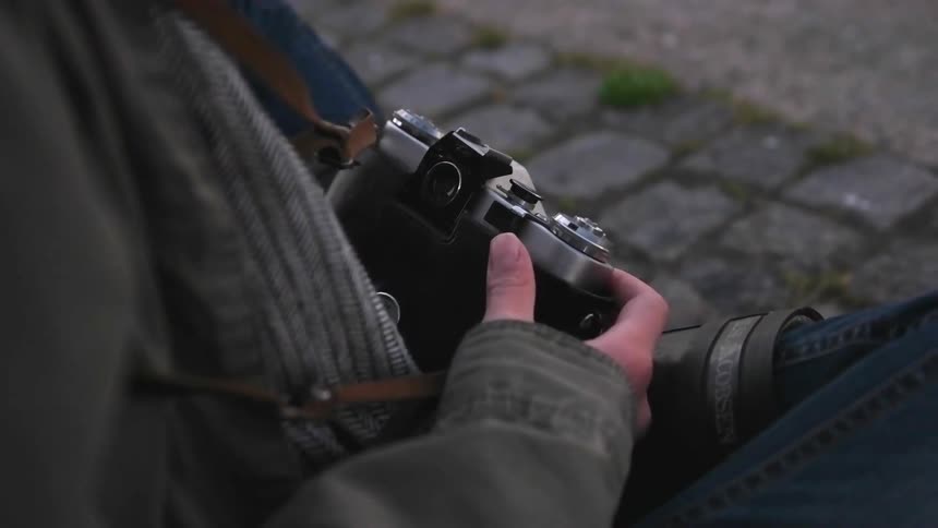 A woman sits with legs crossed holding a film camera