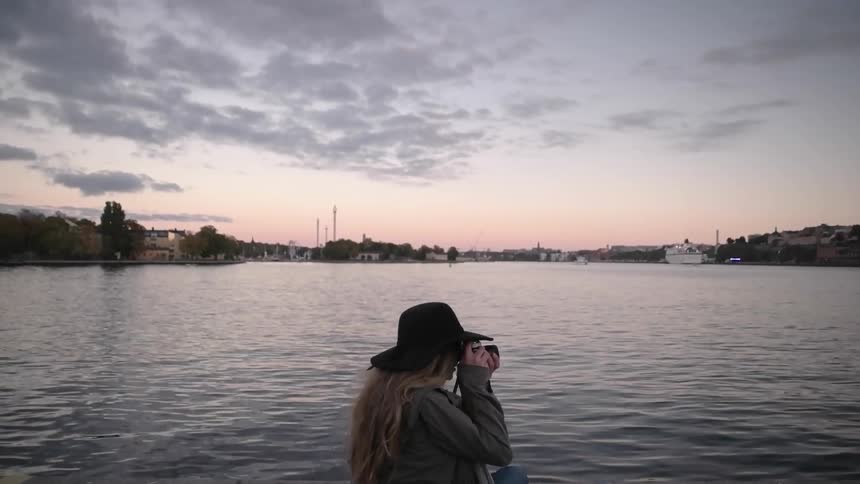 A woman in a cowboy hat photographs near a lake