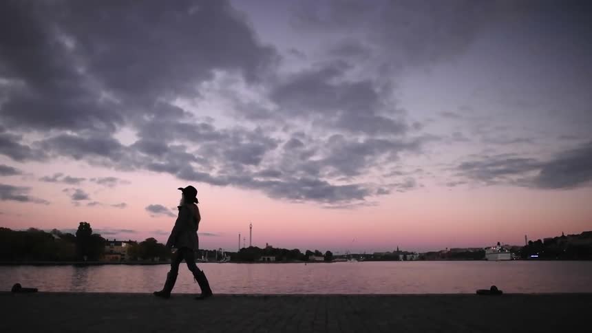 A woman taking photographs near a body of water at sunset