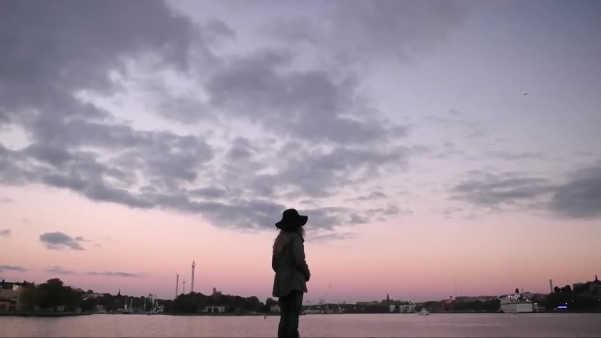 A woman is standing outside by the water watching the sun set