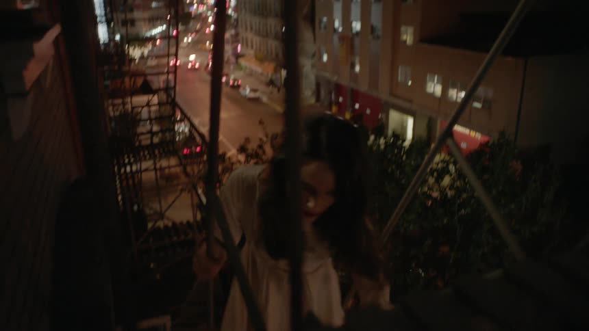Woman in dress stepping down a fire escape on a city building