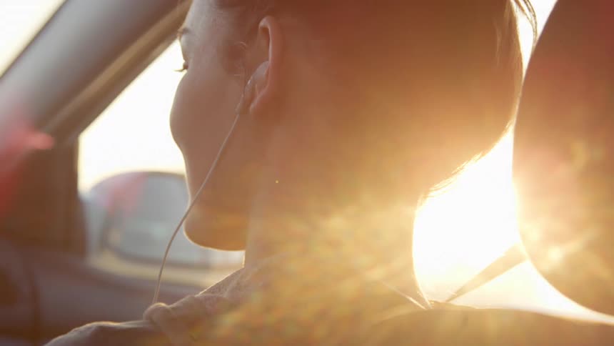 Woman wearing earbuds travels in the passenger seat of a vehicle on a sunny day