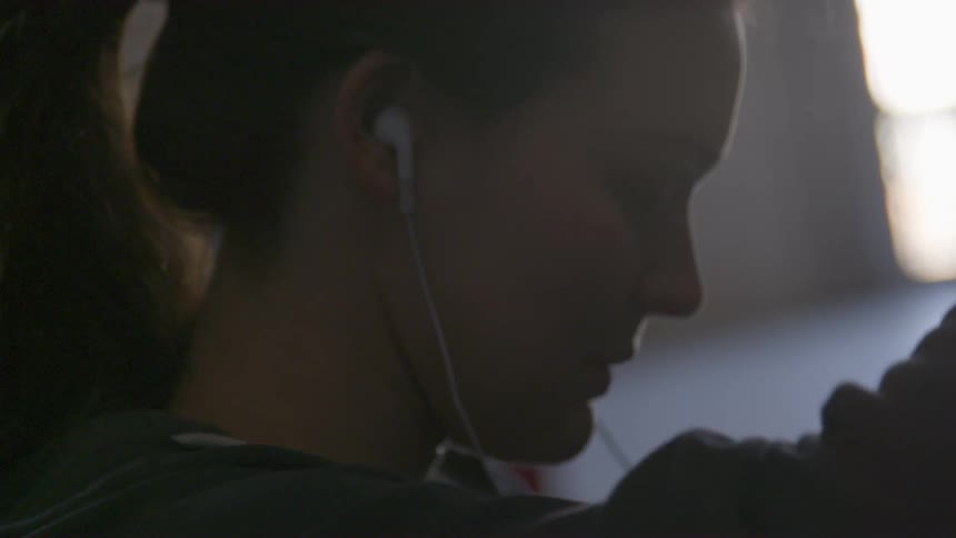 Woman with a long sleeve t shirt and white earphones raises her arms