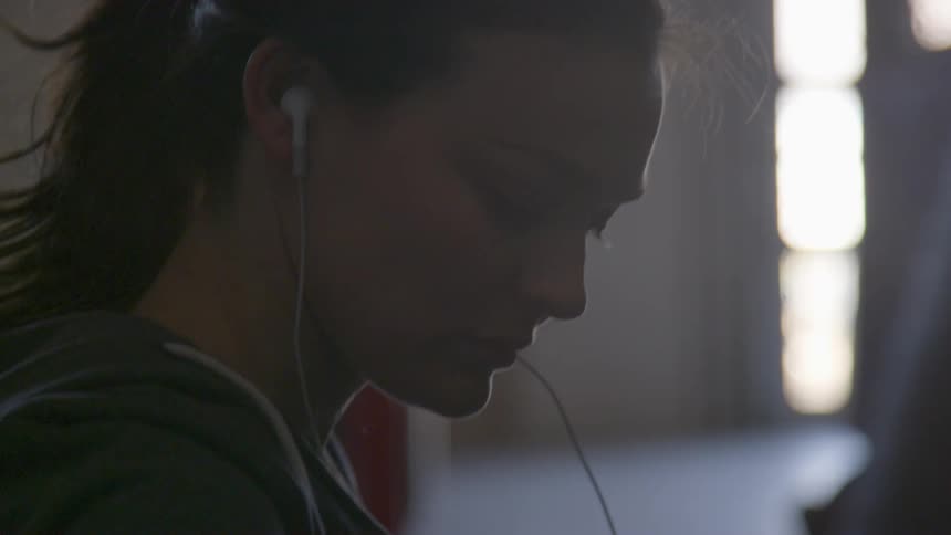 A woman with earbuds sitting on the floor with fingerless gloves