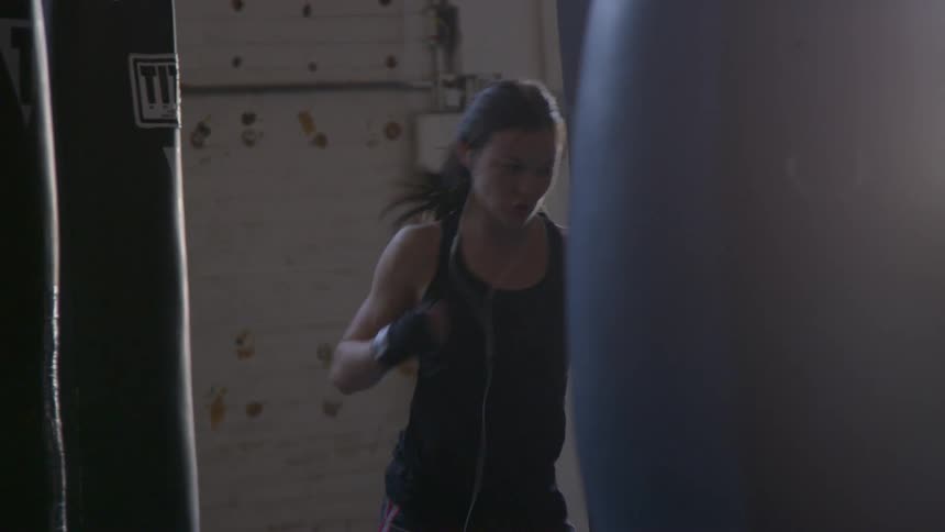 A woman uses wrapped hands to punch a bag in a gym