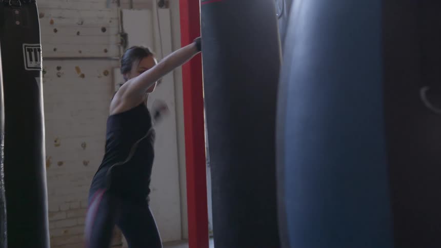 A female athlete practices punching and kicking a large bag in a gym