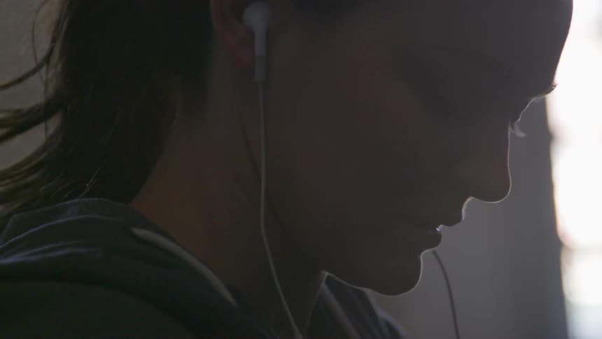 Woman wearing earbuds looks down towards the floor