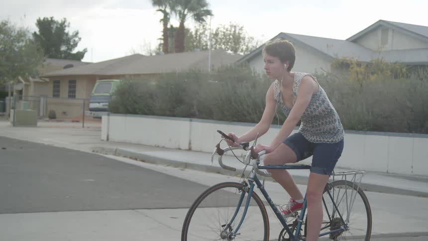A teenager bikes through a neighborhood while looking at her cell phone