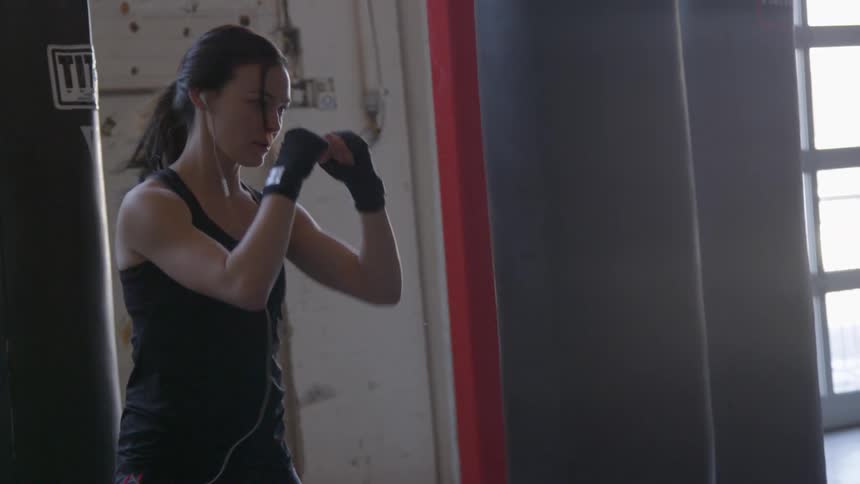 Woman with ponytail and hits a heavy bag in the gym