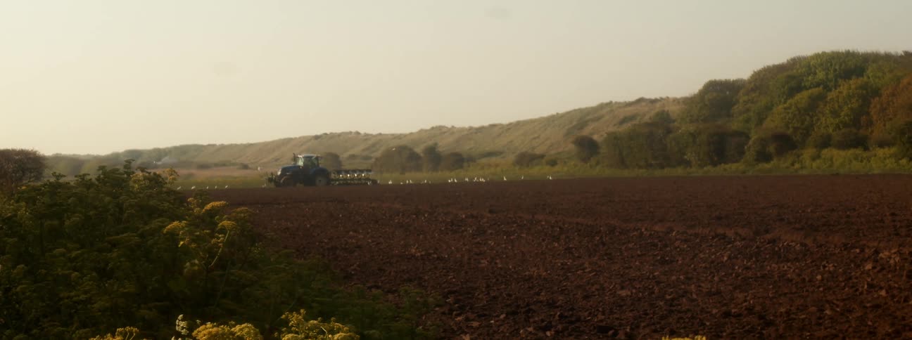 Tractor moves along empty earthen field between hills
