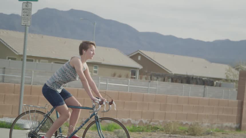A white female teenager rides a bike through a neighborhood