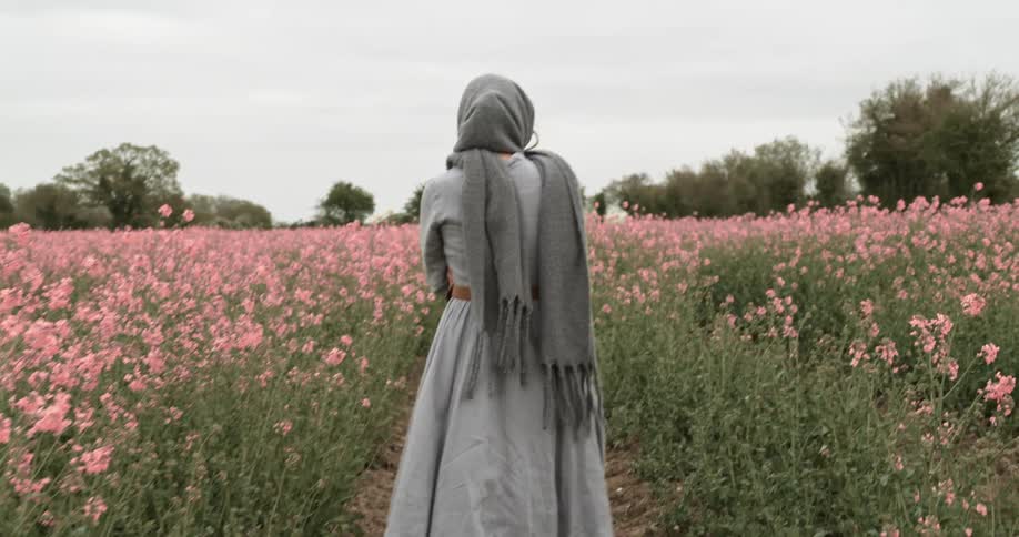 Woman wearing a shawl over her head walking through a field of pink flowers