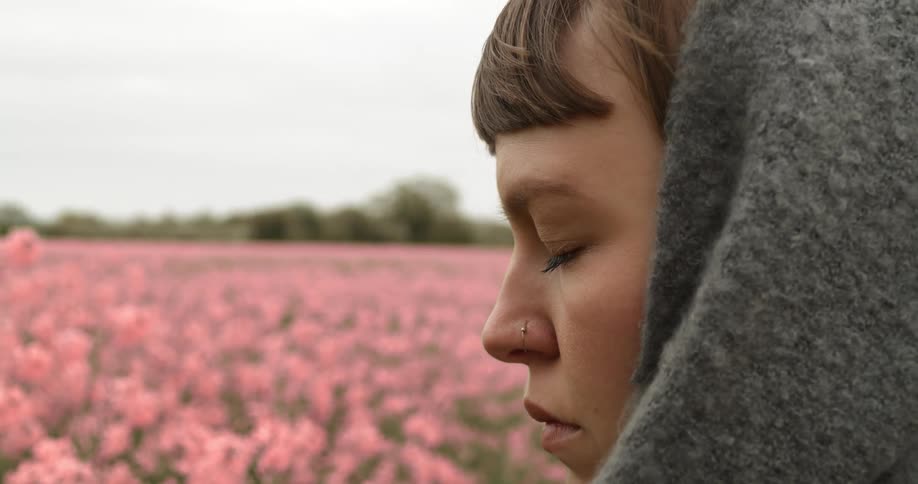 A teenager stands in a field of flowers with her eyes closed