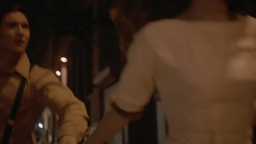 A man and woman are running down a sidewalk at night