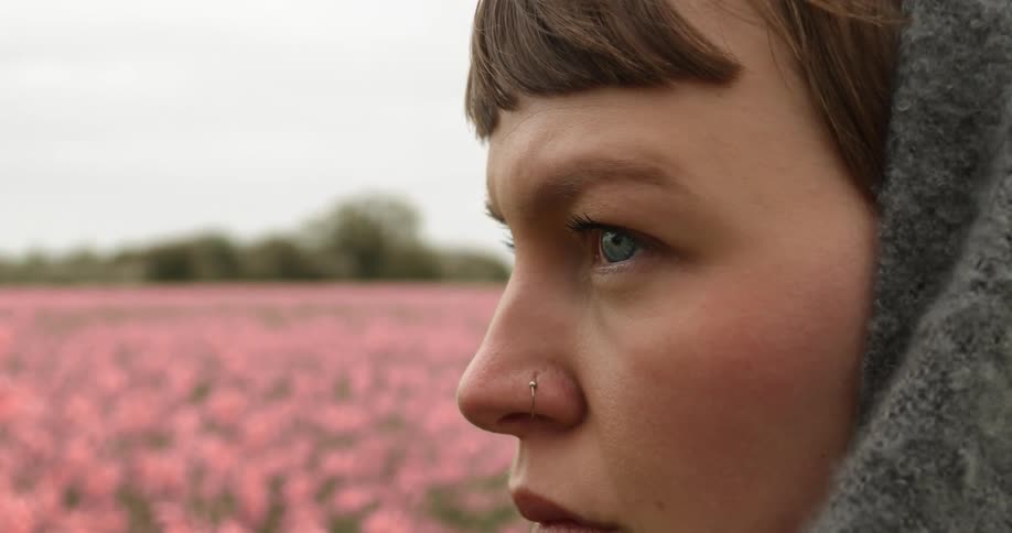 A woman wearing a hood is standing in a flower meadow