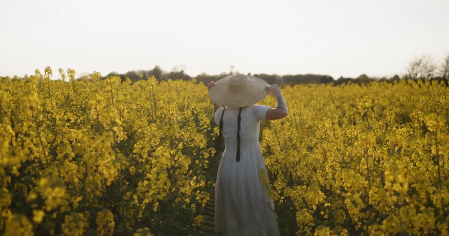 Woman with braided hair and wearing a sunhat walks through a field of vegetation