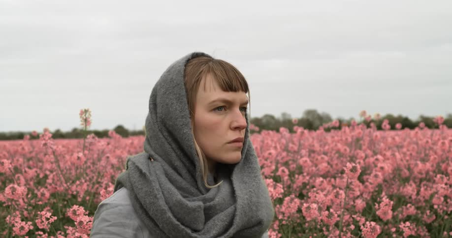 A white woman stands in a field of pink flowers