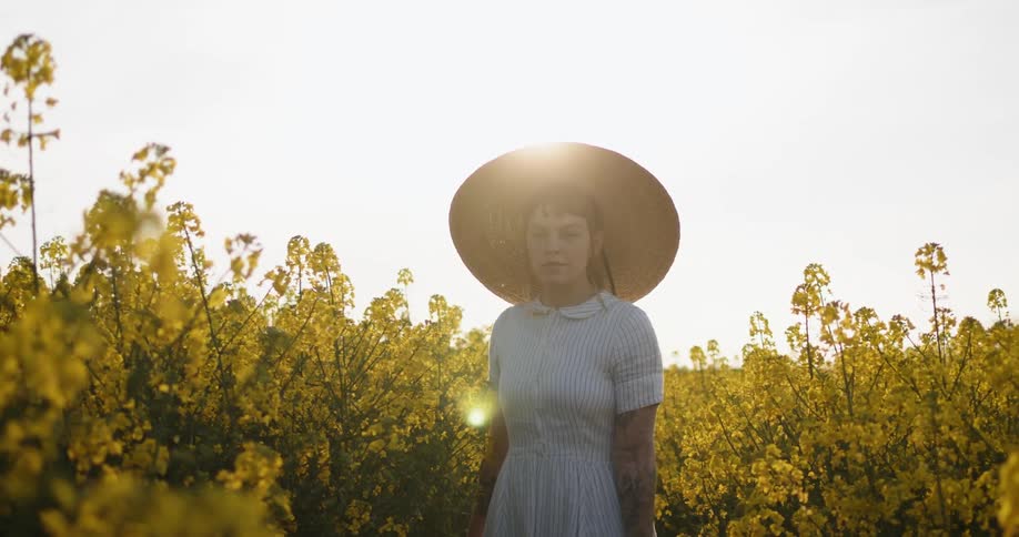 Woman wearing dress and sun hat walks through wild yellow flowers