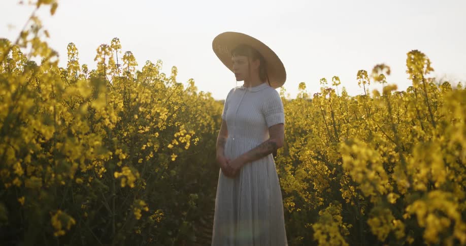 Woman wearing white straw sun hat and white dress stands in field of yellow flowers