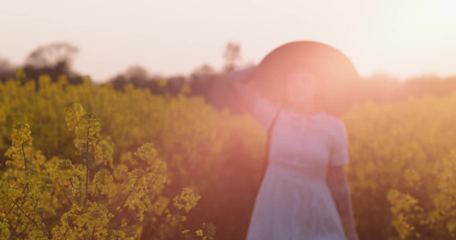 A woman walks through a field of flowers in a white dress and hat