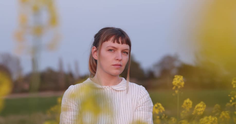Young woman standing on a field of wild flowers looks at the camera