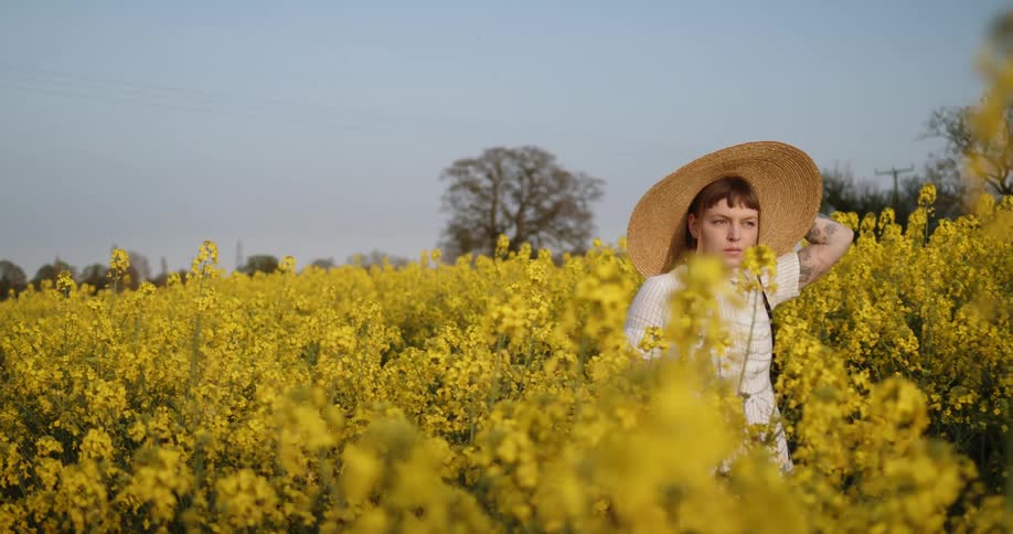 A woman walking through a meadow with flowers with trees and the sky in the background
