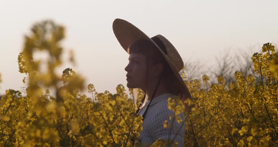Woman wearing a sunhat turns her head as she stands in a field of floral vegetation