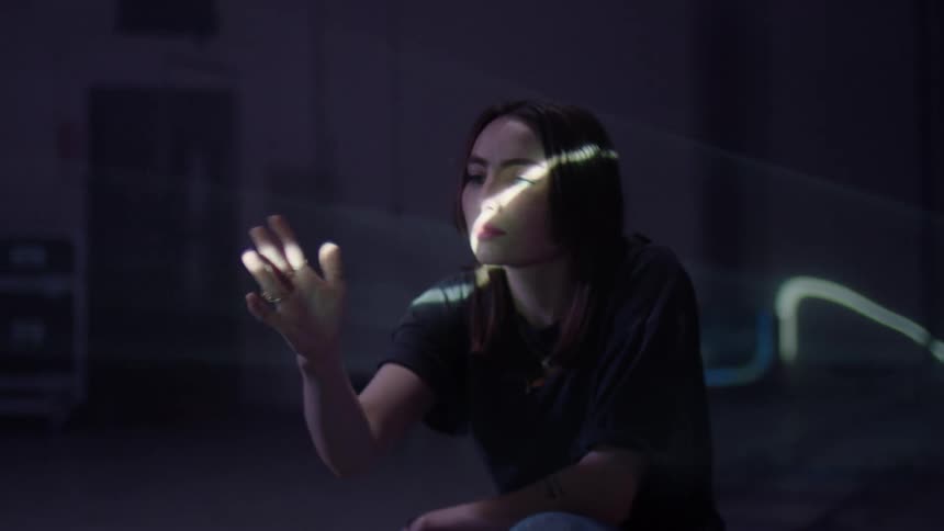 A white woman kneels and twists her hand around in a beam of light