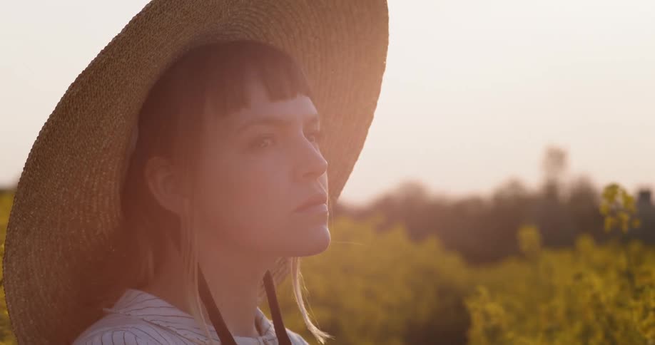 A young woman in a sun hat standing outdoors among tall plants