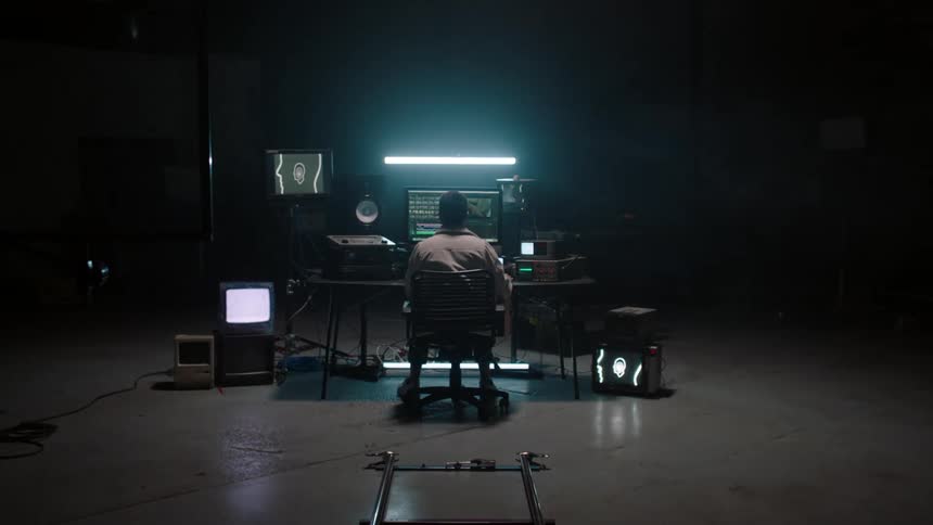 Man sits at a desk surrounded by electronic equipment