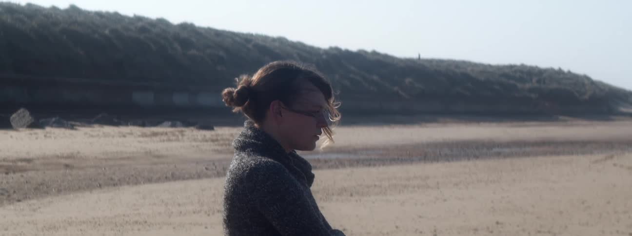 Young woman wearing a sweater stands on the sands of a beach