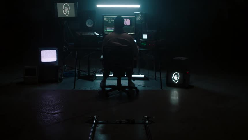 A man sits at the computer in the dark room