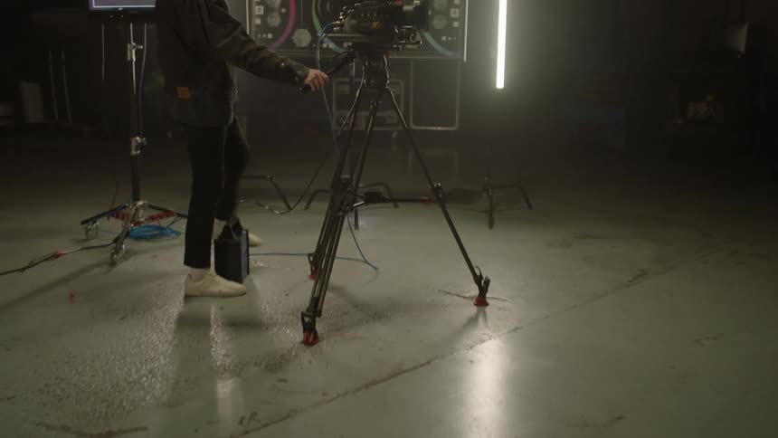 A white man walks into a room and gets behind a film camera