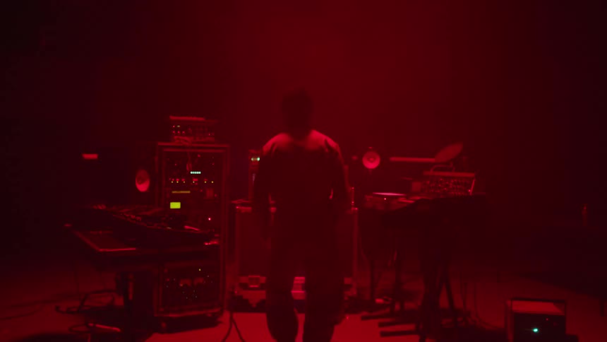 A black musician jumps near a bank of instruments and machines