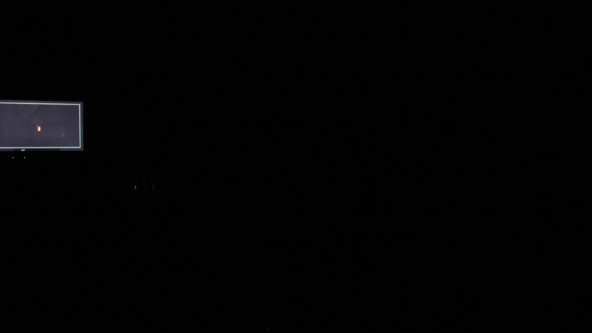 A man looks through the lens of a camera on a tripod as monitors and lights flash and strobe around him