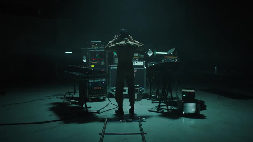 Musician surrounded by electronic equipment in a dimly lit room