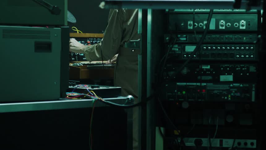 A white man fiddles with a machine covered in buttons and dials
